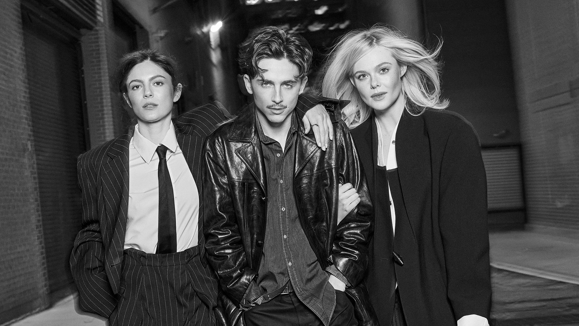Timothee Chalamet, Elle Fanning and Monica Barbaro were photographed in New York City on November 23rd 2024. Monica, left, Sportmax pinstripe jacket, white shirt, pants; Turnbull and Asser silk tie; Bulgari ring; Christian Louboutin boots. Hair by Jacob Rosenberg, Makeup by Samantha Lau Timothee, center, Celine leather jacket, jeans, boots; CK vintage shirt. Styling by Taylor McNeill, Grooming by Jamie Taylor. Elle, right, Louis Vuitton coat, shirt dress, skirt; Gianvito Rossi boots. Hair by Alissa Frum, Makeup by Tyron Machhausen Artistic and Fashion Director Alison Edmond